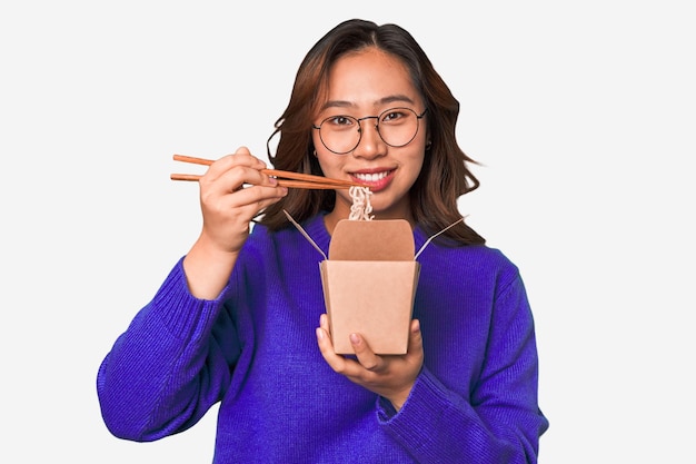 Saboreando macarrão delicioso para viagem, jovem asiática gosta de sua refeição