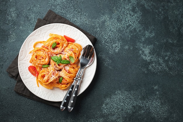 Saborosa apetitosa massa tagliatelle italiana clássica com molho de tomate, queijo parmesão e manjericão no prato na mesa escura. Vista de cima, horizontal. Vista superior com espaço de cópia.