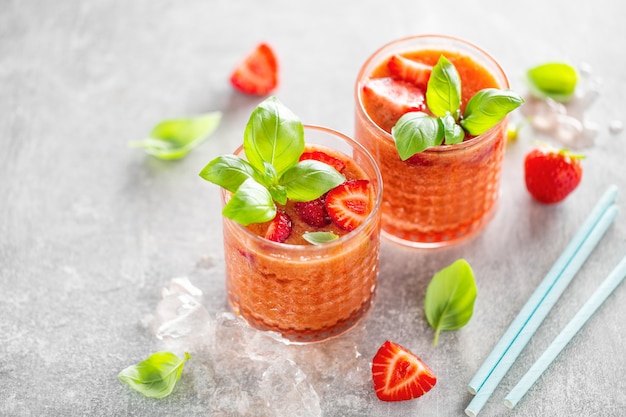 Saborosa bebida fresca com stawberry e manjericão servido em copos na mesa de concreto.
