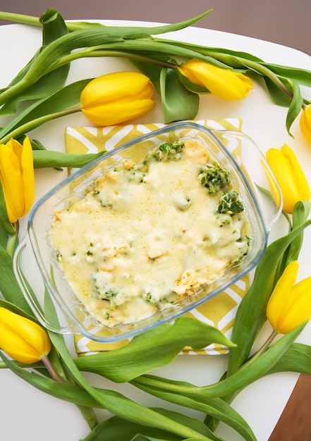 Saborosa caçarola com brócolis, queijo e creme rodeada de tulipas amarelas