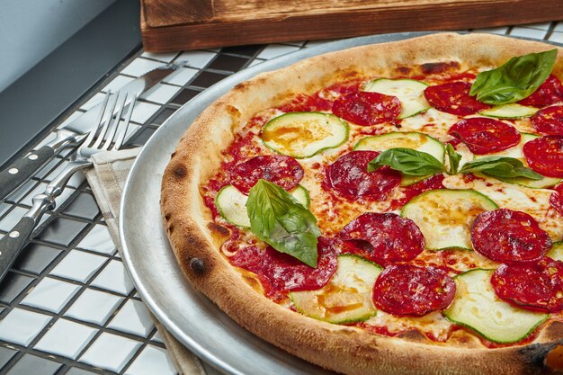 Saborosa pizza com salame, abobrinha e manjericão em uma mesa branca. Cozinha tradicional italiana. Comida deliciosa plana leigos. Vista do topo