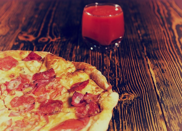 Saborosa pizza de calabresa com cobertura variada e queijo na mesa de madeira perto de um copo com suco de tomate