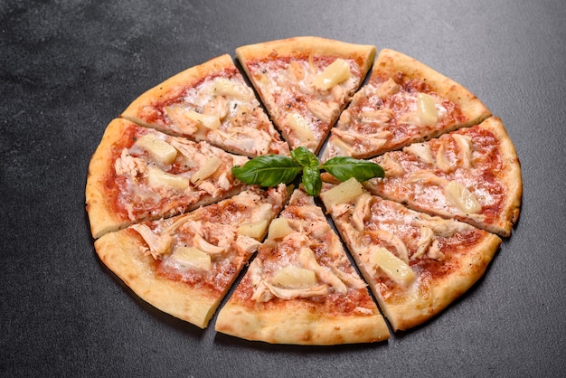 Saborosa pizza de forno com tomate, queijo e abacaxi em um fundo escuro de concreto