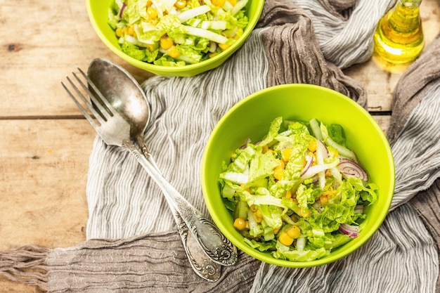 Saborosa salada vegana de repolho chinês, milho doce, cebola roxa e molho. Fundo de madeira, talheres, guardanapo vintage, estilo rústico, vista superior