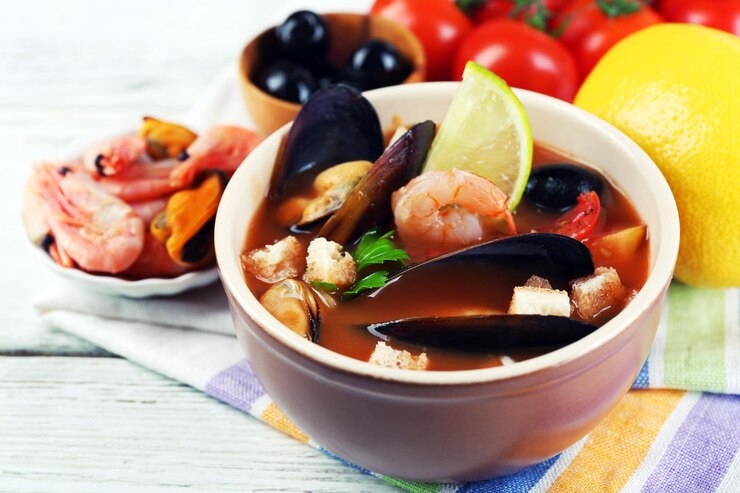 Foto saborosa sopa com camarões, mexilhões, tomates e azeitonas pretas em tigela sobre fundo de madeira
