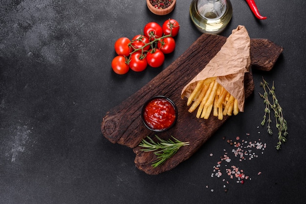 Saborosas batatas fritas frescas e molho vermelho em uma tábua de madeira. Alimentos não saudáveis, fast food