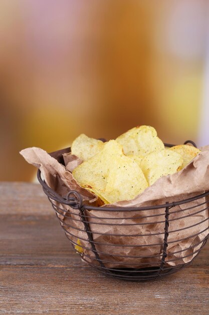 Saborosas batatas fritas na cesta de metal na mesa de madeira sobre fundo claro