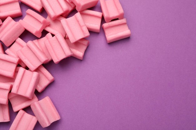 Saborosas pastilhas elásticas cor-de-rosa sobre fundo roxo, espaço plano para texto