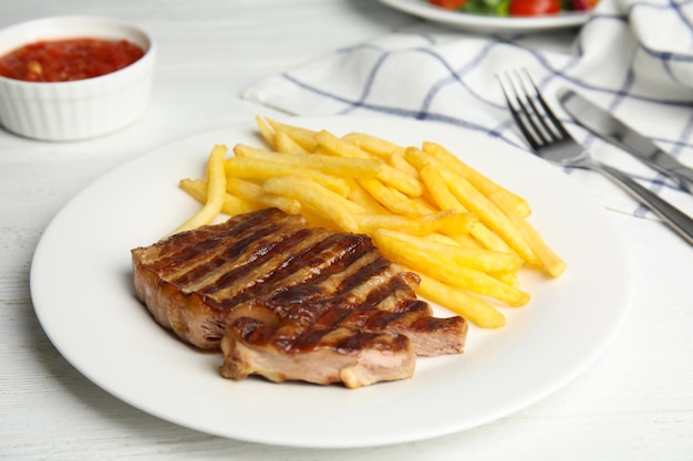 Saboroso bife grelhado e batatas fritas na mesa de madeira branca