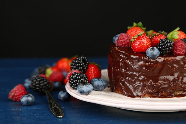 Saboroso bolo de chocolate com bagas diferentes na mesa de madeira em fundo escuro