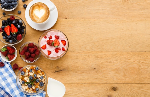 Saboroso café da manhã com iogurte grego leve, muesli, frutas orgânicas frescas e café com leite. Refeições matinais com baixo teor de gordura e início de dia saudável. Conceito de desintoxicação e dieta, vista superior, copie o espaço