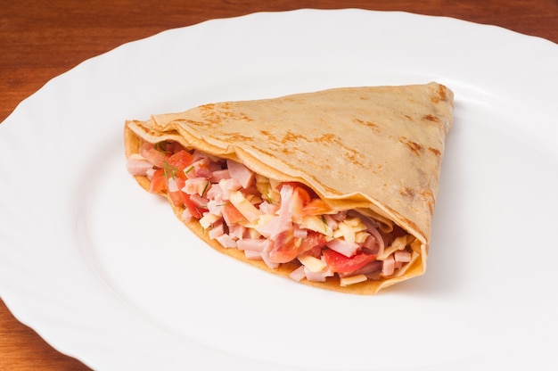 Saboroso crepe com tomate, presunto e queijo em um prato branco