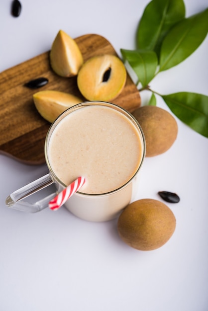 Saboroso e saudável chickoo, chikoo ou sapota milkshake. é uma fruta saudável misturada com leite e gelo servida em copo sobre fundo colorido ou de madeira. foco seletivo