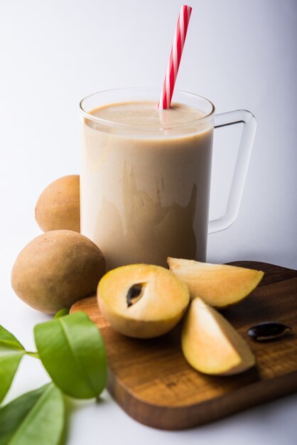 Saboroso e saudável Chickoo, Chikoo OU Sapota Milkshake. É uma fruta saudável misturada com leite e gelo servida em copo sobre fundo colorido ou de madeira. Foco seletivo