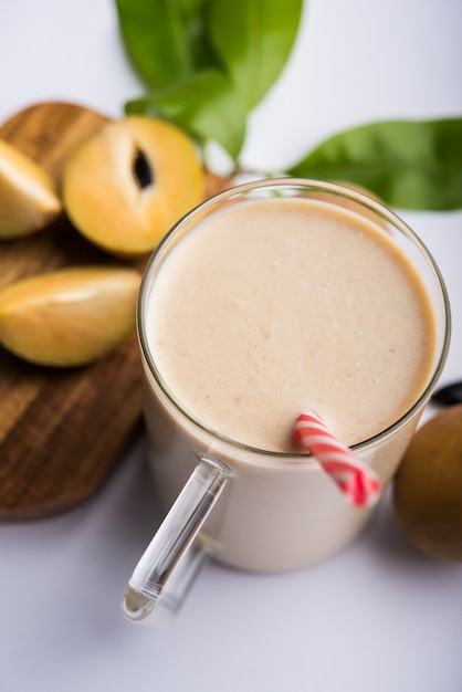 Saboroso e saudável Chickoo, Chikoo OU Sapota Milkshake. É uma fruta saudável misturada com leite e gelo servida em copo sobre fundo colorido ou de madeira. Foco seletivo