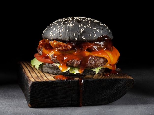 Foto saboroso hambúrguer artesanal com pão preto no fundo preto