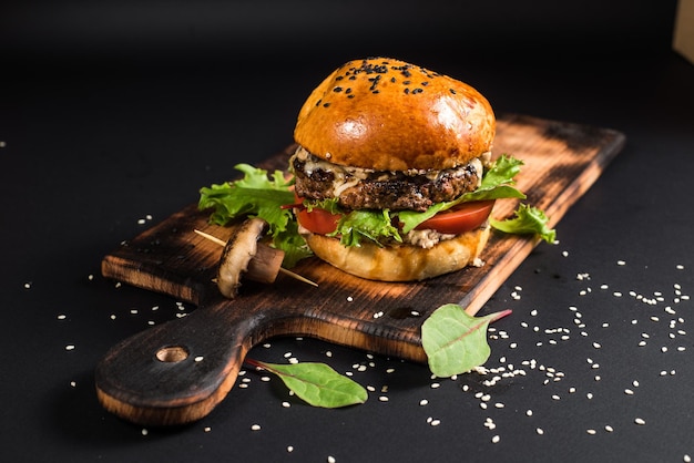 Saboroso hambúrguer com carne grelhada e cogumelos no fundo preto