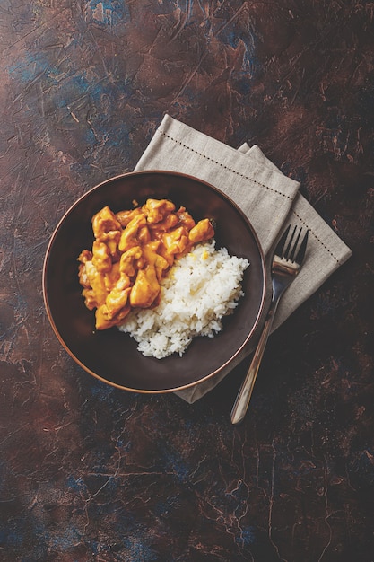 Saboroso jantar com Frango ao molho de curry de leite de coco com arroz em prato escuro, vista de cima. Estilo asiático.