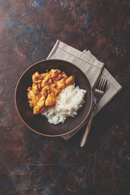 Saboroso jantar com frango ao molho de curry de leite de coco com arroz em prato escuro, vista de cima. estilo asiático.