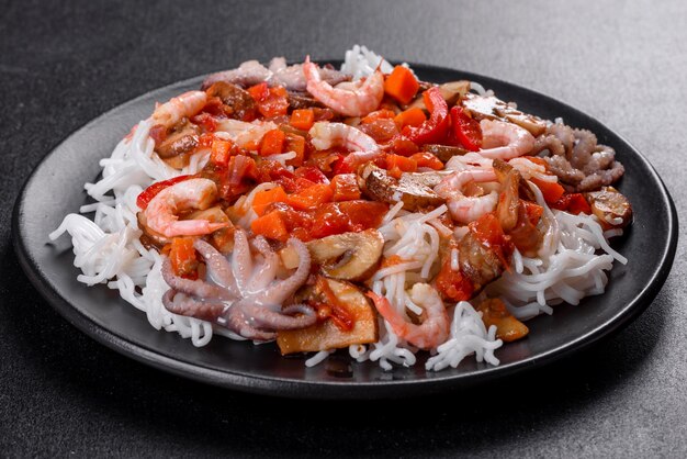 Saboroso macarrão de arroz com tomate, pimenta vermelha, cogumelos e frutos do mar em um fundo escuro de concreto