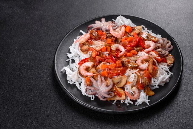 Saboroso macarrão de arroz com tomate, pimenta vermelha, cogumelos e frutos do mar em um fundo escuro de concreto