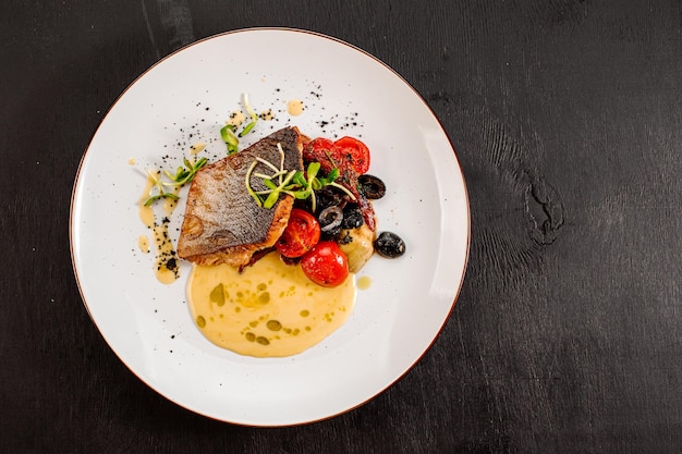 Foto saboroso peixe dourado grelhado com legumes cozidos e molho em fundo de madeira