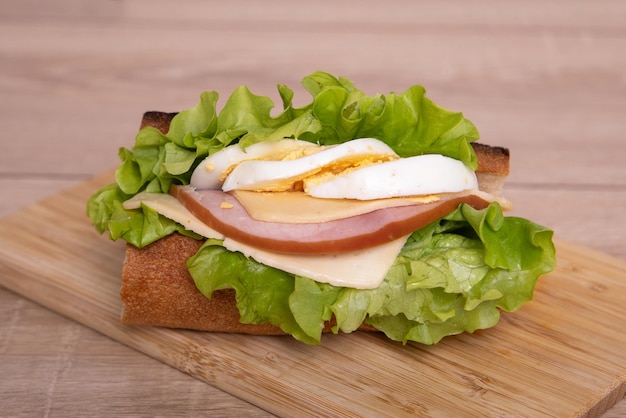 Saboroso sanduíche com presunto, queijo, ovos e saladas verdes em fundo de madeira