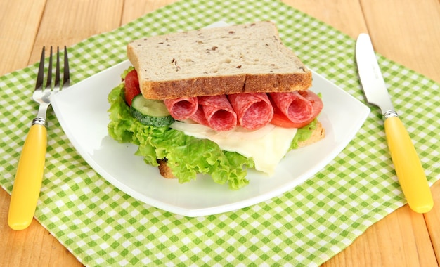 Saboroso sanduíche com salame e legumes na chapa branca sobre fundo de madeira