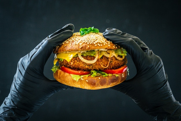 Saboroso sanduíche de hambúrguer nas mãos com luvas pretas