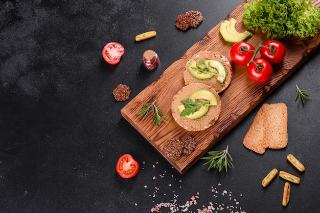 Saboroso sanduíche fresco com pasta de fígado, pedaços de abacate e uma rúcula em uma mesa de concreto escura