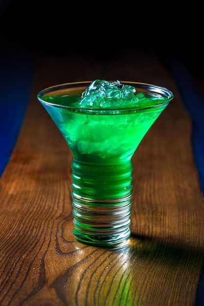 Saboroso smoothie verde alcoólico com gelo picado em uma mesa de madeira. Cocktail de verão relaxante. Espaço para texto.
