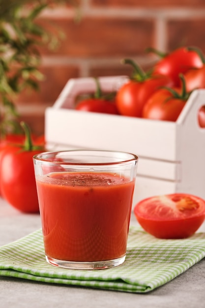 Saboroso suco de tomate em um copo com tomates vermelhos maduros.