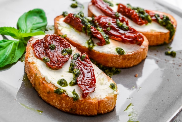 Saborosos aperitivos italianos salgados, ou bruschetta, em fatias de baguete tostada, guarnecidas com manjericão