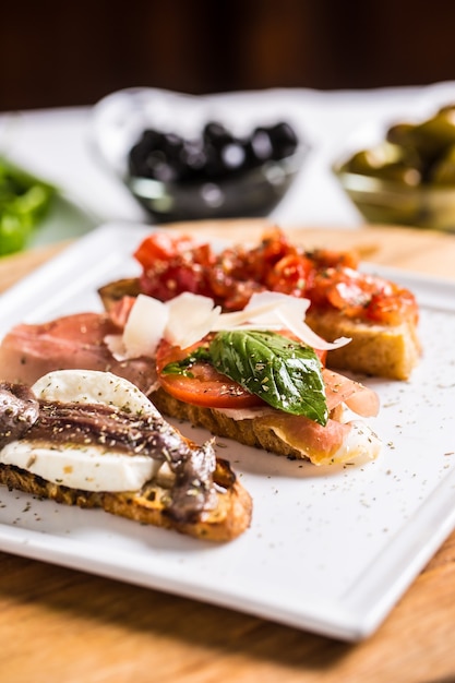 Saborosos bruschettes de aperitivo italiano com tomate anchovas prosciutto e mussarela.