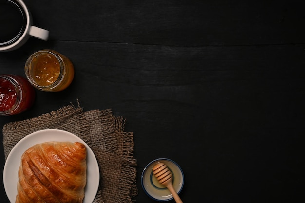 Saborosos croissants amanteigados com compotas de mel e café na mesa de madeira preta no café da manhã