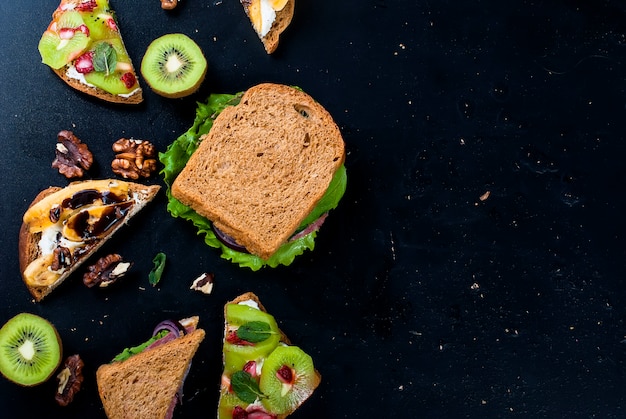 Saborosos doces sanduíches com bananas, nozes e chocolate, kiwi, morangos e hortelã em fundo preto