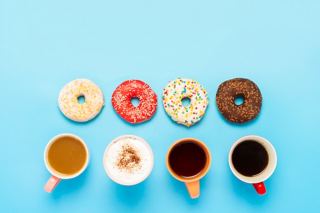 Saborosos donuts e copos com bebidas quentes em um espaço azul. conceito de doces, pastelaria, pastelaria.