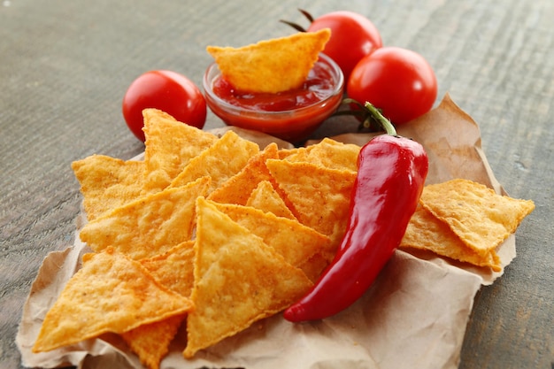 Saborosos nachos tomates vermelhos e pimenta em papel sobre fundo de madeira