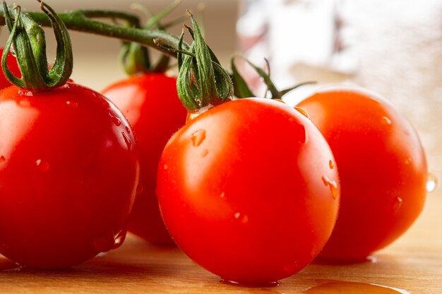 Saborosos tomates vermelhos crus no galho coberto com gotas de água caindo na placa de madeira deles