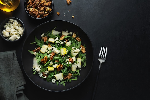 Sabrosa y apetitosa ensalada con pera, queso azul, nueces, rúcula servida en un plato oscuro.