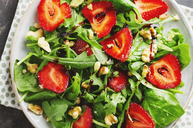 Foto sabrosa apetitosa ensalada de verano recién hecha con rúcula, fresa y nueces servido en un tazón. de cerca