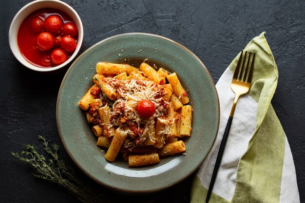 Sabrosa apetitosa pasta italiana clásica con salsa de tomate, queso parmesano y fideos en un plato sobre una mesa oscura. Vista superior, horizontal. Pasta italiana. Pasta penne en salsa de tomate con pollo, tomates.