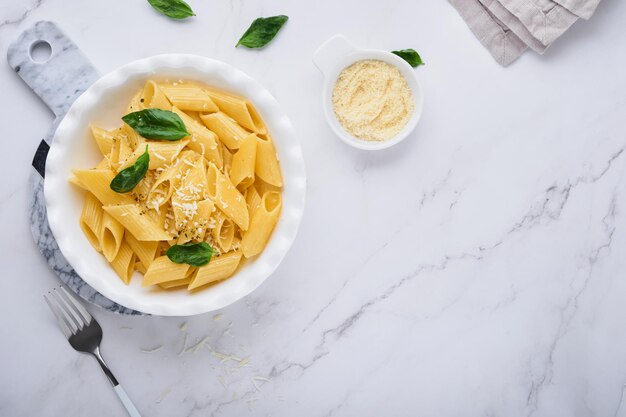 Sabrosa y apetitosa pasta penne italiana clásica con queso parmesano y albahaca en un plato blanco sobre un plato sobre una mesa de piedra. Plato tradicional de la cocina italiana. Vista superior.