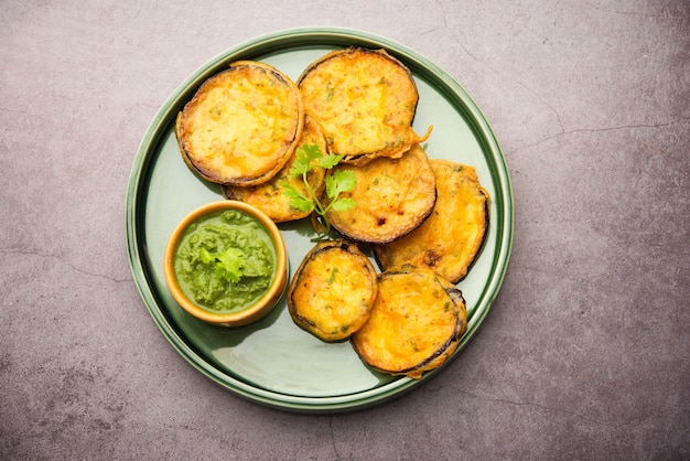 Sabrosa berenjena Pakora o crujientes buñuelos de berenjena, merienda india a la hora del té servida con chutney verde