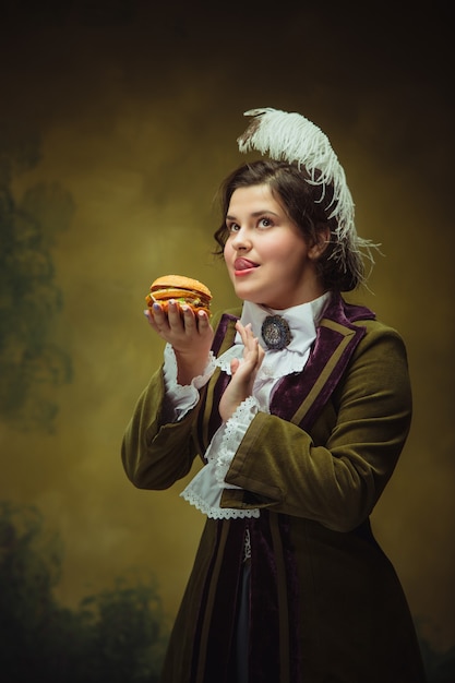 Sabrosa comida rápida. Aspecto de moda moderno, retrato de mujer hermosa del período renacentista. Estilo retro, comparación del concepto de eras. Modelo de mujer caucásica como personaje histórico clásico, anticuado.