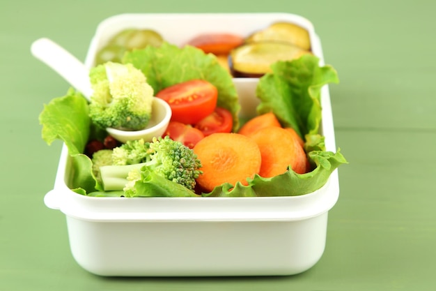 Sabrosa comida vegetariana en una caja de plástico en una mesa de madera verde
