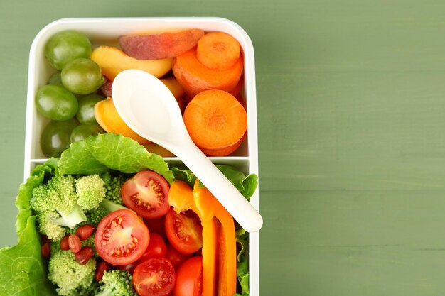 Sabrosa comida vegetariana en una caja de plástico en una mesa de madera verde