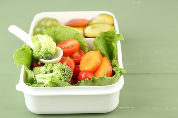 Sabrosa comida vegetariana en una caja de plástico en una mesa de madera verde