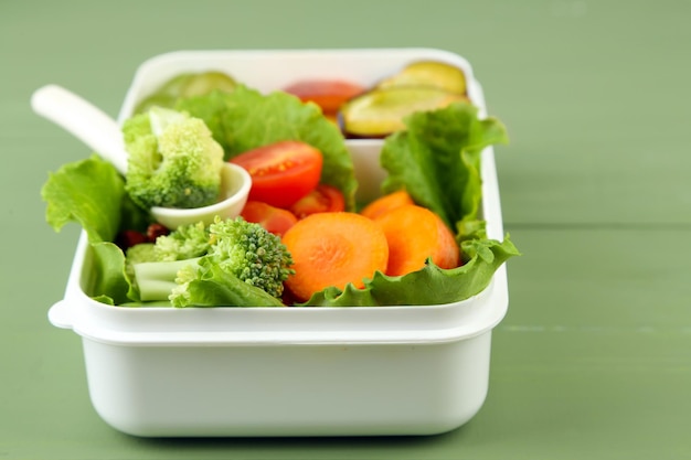 Sabrosa comida vegetariana en una caja de plástico en una mesa de madera verde