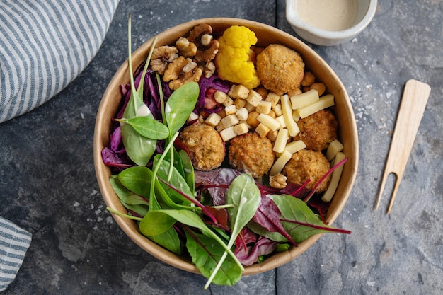 Sabrosa ensalada vegetariana vegana con garbanzos, falafel y hojas servidas en un tazón de papel. Concepto de vida saludable o cero desperdicio